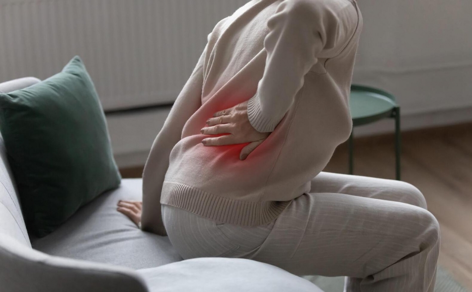 eine Frau beim aufstehen mit der Hand am schmerzenden Rücken